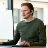 Man sitting at desk in office wearing Aftershokz OpenComm headset